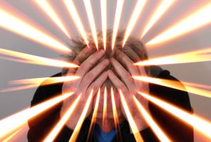 Man holding head in hands with beams of light appearing to radiate from head and hands